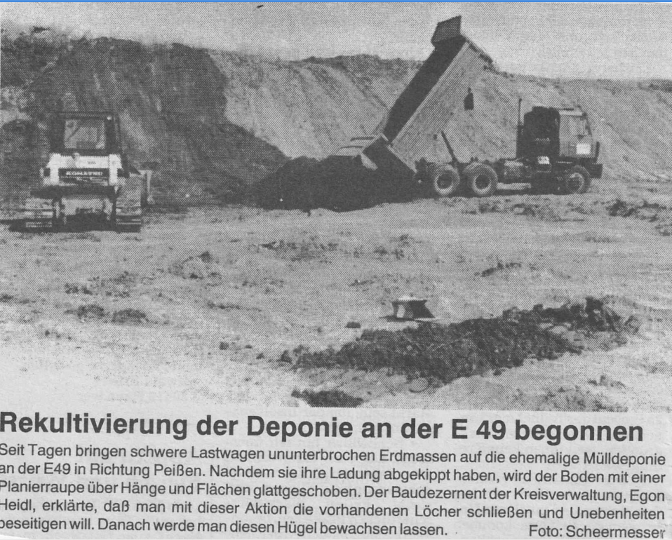 Im Bild ist die stillgelegte Deponie und davor eine Planierraupe und ein LKW-Kipper in Bernburg (Saale) zu sehen. 1995 wurde der erste Mutterboden mit LKW-Kippern angefahren und mit schwerer Technik darauf verteilt.